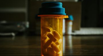 A prescription bottle filled with pills against a dimly lit background.