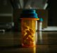 A prescription bottle filled with pills against a dimly lit background.