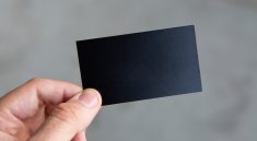 A person holding a plain black business card in a minimalistic setting.