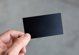 A person holding a plain black business card in a minimalistic setting.