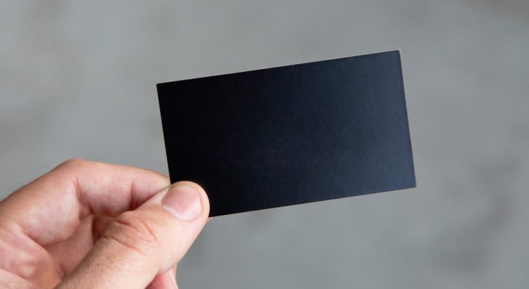 A person holding a plain black business card in a minimalistic setting.