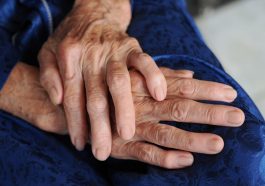 Close-up of elderly hands resting on a lap, showcasing signs of aging and care.