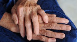 Close-up of elderly hands resting on a lap, showcasing signs of aging and care.
